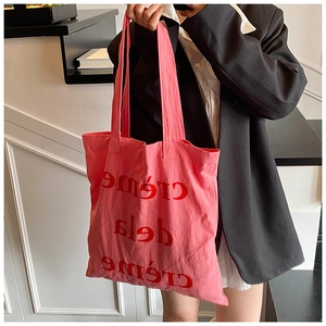 Détail d'un sac cabas en toile rose avec slogan rouge et larges anses pour femmes