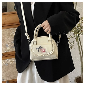 Close-up of cream white Boston bag with lace edges, ribbon bow, and rabbit patch detail