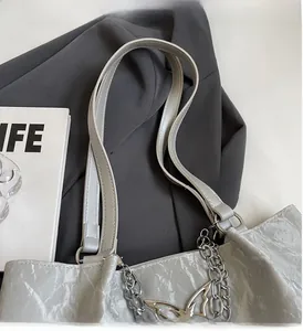 Detail of silver wavy tote bag featuring a metallic chain and butterfly pendant ornament