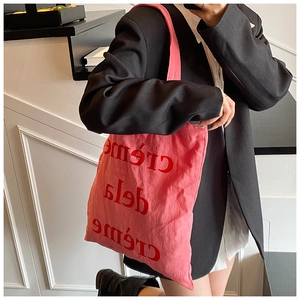 Sac cabas en toile rose avec texte rouge porté par un mannequin en costume chic