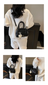 Detail of black leather handbag featuring pearl heart charm and metal zippers