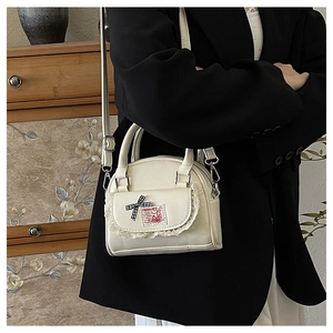 Detail of a beige mini Boston bag featuring white lace trim and a black plaid ribbon bow