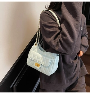 Detail of mint green quilted shoulder bag with gold chain strap on model's side