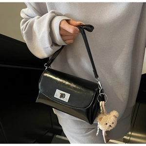 Detail of glossy black leather underarm bag with silver twist lock and plush bear charm