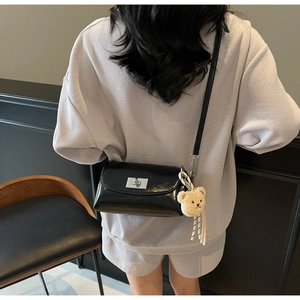 Detail of black glossy pillow bag with silver buckle and brown bear charm on gray outfit