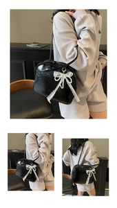 Detail of black faux leather shoulder bag with white lace and pearl bow charm accessory
