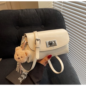 Detail of cream faux leather crossbody bag featuring a silver twist lock and bear charm