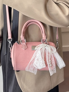 Pink woven boston bag with large lace bow and pearl charm worn by model in beige suit
