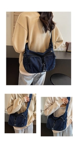 Detailed macro view of dark blue denim shoulder bag featuring front zipper pockets and texture