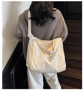 Detail of off-white hobo bag featuring textured fabric and decorative lace ribbon
