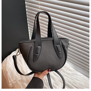 Detailed view of black woven texture handbag with sleek gold metal hardware and wide handle