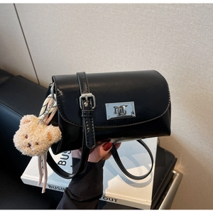 Detail of black faux leather crossbody bag with silver twist lock and beige plush bear charm