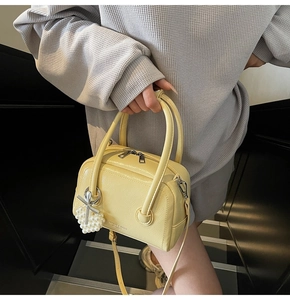 Close-up of bright yellow Boston bag with leather texture and pearl bow charm detail