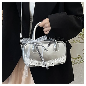 Detail view of silver glossy Boston bag with white lace edges and a checkerboard bow charm