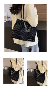 Detail of black tote bag featuring wave textures, silver chains, and butterfly charm