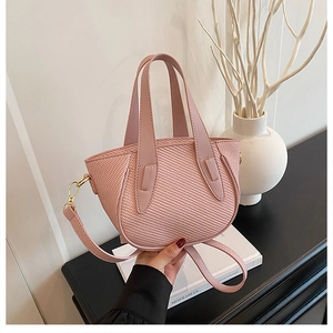Pink woven bucket bag featuring rounded base and adjustable shoulder strap detail