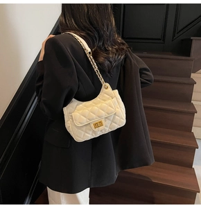 Close-up of beige quilted shoulder bag with gold hardware on model's shoulder