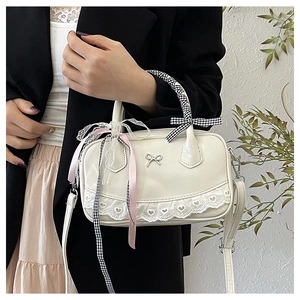 Close-up of cream PU leather boston bag with heart lace, bow detail and checkered handle