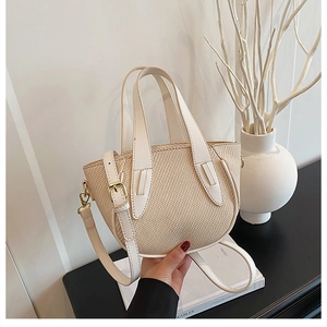 Detailed close-up of beige woven bucket bag with white leather straps and gold hardware