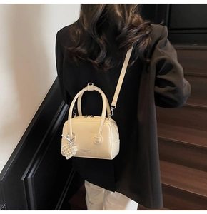 Detail view of beige Boston bag with pearl heart charm and textured leather finish