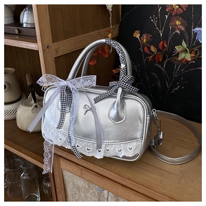 Close-up of silver Boston bag featuring a metal bow, lace trim and checkered ribbon detail