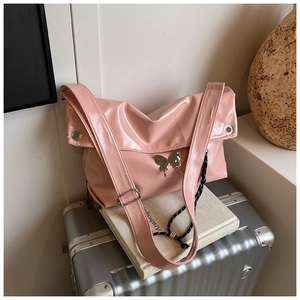 Gros plan du sac cabas en cuir souple rose brillant avec détail papillon en métal sur valise