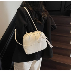 Close-up of cream white underarm bag with lace pearl bow charm and glossy leather texture