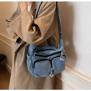 Close-up of denim crossbody bag with multiple zip pockets and fringe detail worn by model