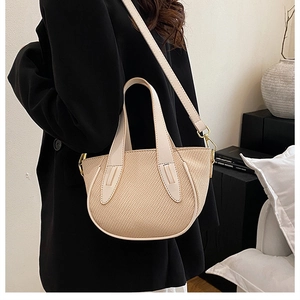 Detail of minimalist cream beige woven bucket bag worn with a black suit for office style