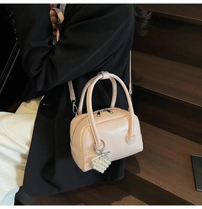 Detail of light beige crossbody bag with pearl heart charm and textured leather finish