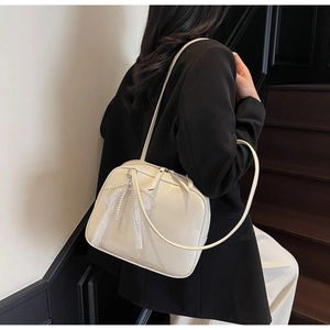 Detail of cream glossy shoulder bag with pearl bow accessory and dual zipper closure