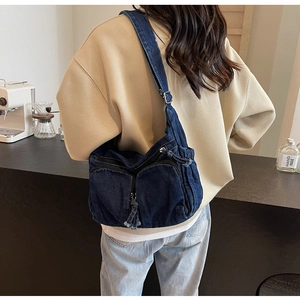 Detail of dark blue denim crossbody bag with dual zipper pockets and fabric tassels