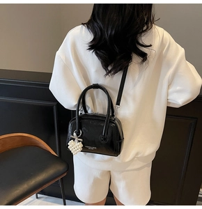 Detail of black patent leather bag featuring a pearl heart charm and bow accent