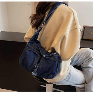 Detailed view of the dark blue denim hobo bag showing zipper pockets and tassel accents