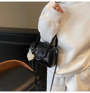 Detail of black glossy handbag featuring pearl heart charm and stylish crossbody strap