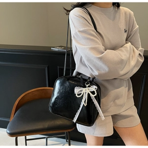 Detail of black glossy shoulder bag with white lace pearl bow charm on a model