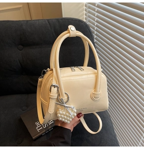 Close-up of cream Boston bag featuring fashion text, gold zipper, and pearl heart charm