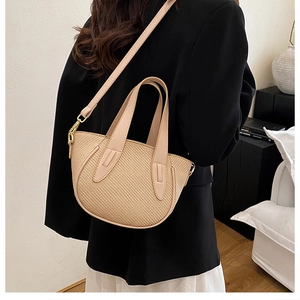 Detail of straw bucket bag with beige woven texture and soft pink leather handle on model