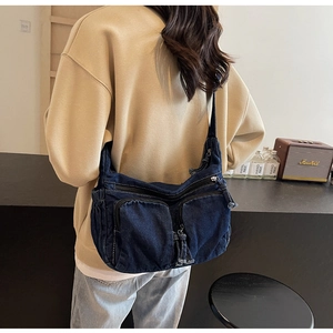 Detail of dark blue denim shoulder bag with utility pockets shown on a model
