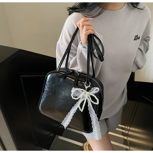 Detail of black underarm pillow bag with white lace and pearl bow charm accessory