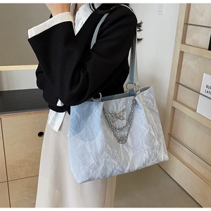 Close-up of light blue wavy tote bag with silver butterfly pendant and metal chains