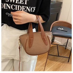 Detail of a brown woven texture bucket bag with leather strap and gold hardware accents