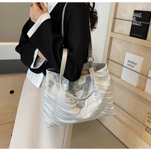 Detail of silver tote bag showing wavy texture and butterfly chain charm in daily use