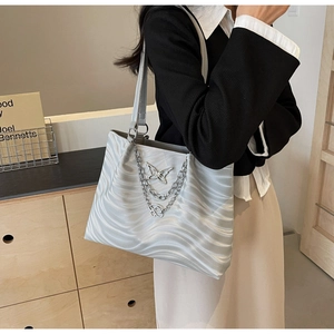Detail of silver tote bag featuring wavy texture and metallic butterfly chain pendant