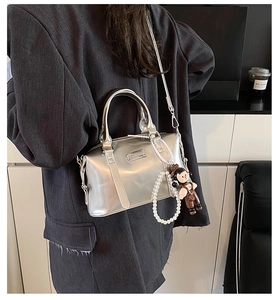 Detail of silver metallic Boston bag with pearl chain and cartoon doll on a model