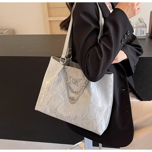 Macro detail of silver tote bag showing wavy pleated texture and butterfly metal charm