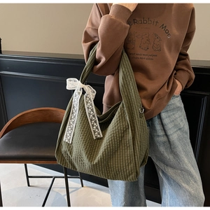Detail view of large green plaid canvas tote bag with white lace bow and wide strap