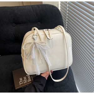 Detail of cream pillow bag featuring pearl bow and lace charm with dual zip closure