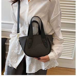 Detail of black woven texture bucket bag with dual handles and gold metal hardware