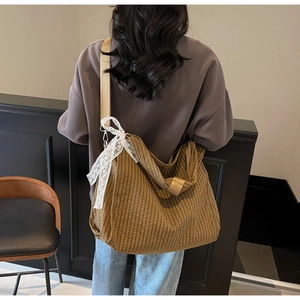 Detail of a brown plaid tote bag with lace bow accent and adjustable wide shoulder strap